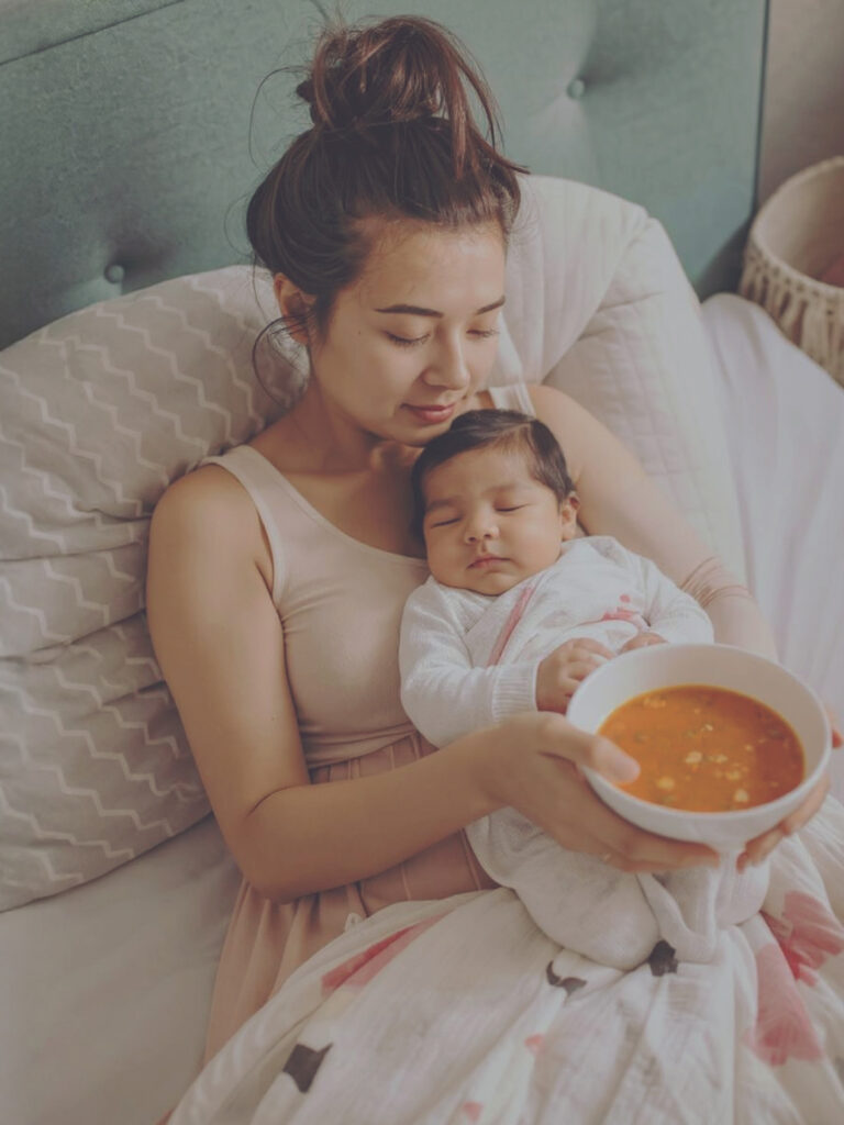 Frisch gebackene Mutter kuschelt mit ihrem Baby, während eine gesunde Mahlzeit von Mothers Finest bereitsteht.